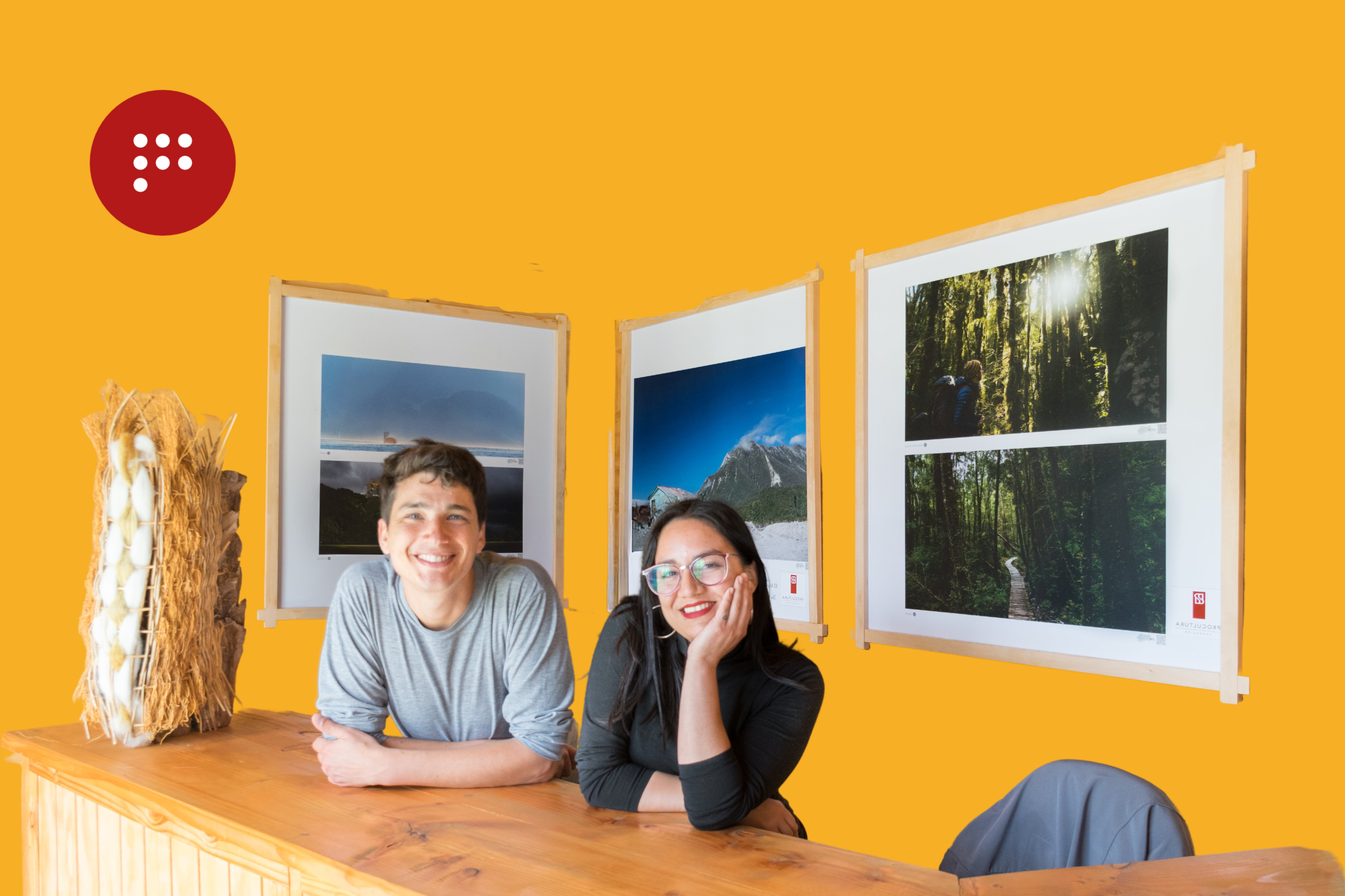 Imagen de una pareja feliz que firmó un contrato de arrendamiento. La pareja está sentada frente a una mesa de madera con un fondo amarillo, en la pared logotipo de Propiedades Punto